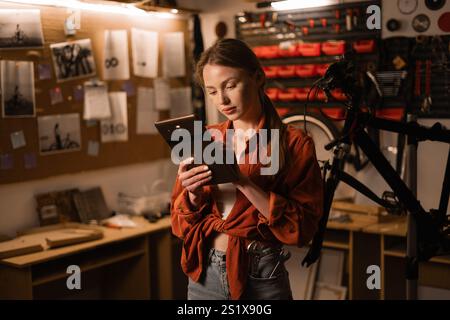 Technology in bicycle repair. Woman mechanic or repairman using a digital tablet in a bicycle repair shop. Stock Photo