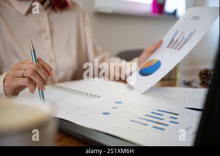 A professional business person or sccountant reviewing charts and graphs on printed reports, focusing on business data and trends in a workspace. Stock Photo