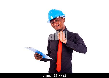 young man engineer wearing blue safety helmet, holding clipboard and loosening his neck tie. Stock Photo