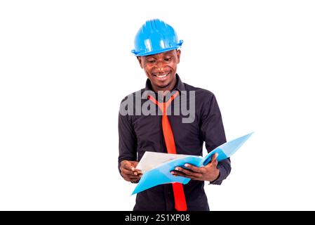 portrait of a young man engineer wearing a hard hat reads and checks documents while smiling. Stock Photo