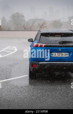 Blue Peugeot 2008 in the rain. Rear view of compact french crossover in parking lot in a city in rainstorm. Stock Photo