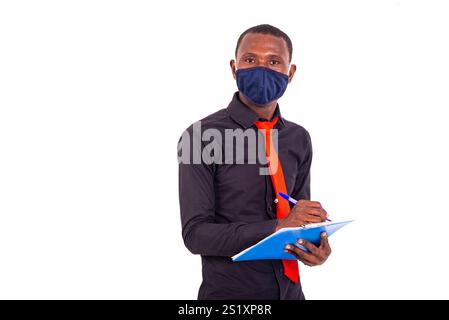 portrait of a handsome young man wearing a fabric medical mask and taking notes in a document on clipboard. Stock Photo