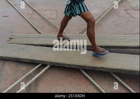 11.11.2015, Yangon, Myanmar, Asia - A man wearing flip-flops walks over wooden gangplanks by the riverfront of the Yangon River (Hlaing River). Stock Photo