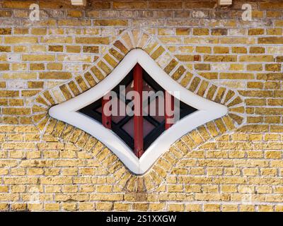 Diamond shaped window with black and dark red muntins, in white wooden frame, in brick facade of old house in Hindeloopen, Friesland, Netherlands Stock Photo