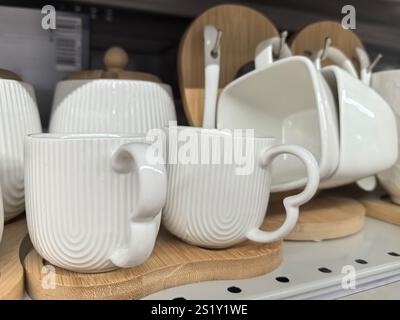 Two charming white mugs with unique handles sit on a wooden platter. Surrounding them are other coordinated kitchen items, creating a cozy and invitin Stock Photo