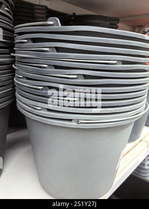 Several gray buckets sit perfectly stacked on a shelf in a home goods store, showcasing organized display and simplicity in design, ready for various Stock Photo