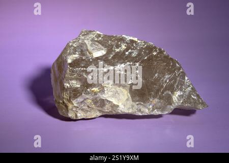 macro photography of natural mineral from geological collection raw clear quartz rock crystal stone on light purple background Stock Photo