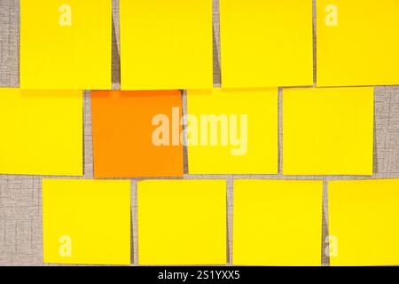 A grey wall covered in empty yellow sticky notes, with one orange Stock Photo