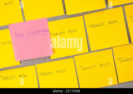 A grey wall with a pink note that says "For everything" on it. There are many other yellow notes on the board, which say "thanks mom". Thank you. Stock Photo