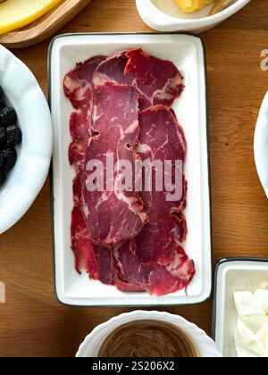 Pastirma Dried Pastrami slices, beef meat with herbs on wooden board. Wooden background. Top view. Ready to eat Stock Photo