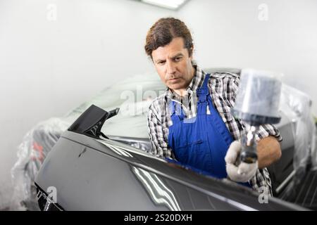 Repairman painter hand in protective glove with airbrush pulverizer painting car body Stock Photo