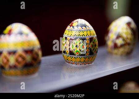 Three colorful eggs are displayed on a shelf. The eggs are decorated with intricate patterns and designs, giving them a unique and artistic appearance Stock Photo