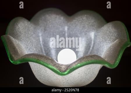 White glass lamp with a green edge and an abstract rounded shape on a black background Stock Photo