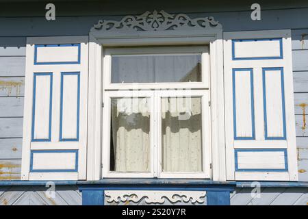 Wooden window with ornate wooden decorations and blue accents on a white background, Budy, BiaNowieZa, Bialowieza, Podlaskie Voivodeship, Podlaskie Stock Photo