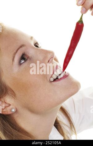 A young woman bites into a chilli pepper. Against a white background Austria Stock Photo
