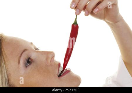 A young woman bites into a chilli pepper. Against a white background Austria Stock Photo