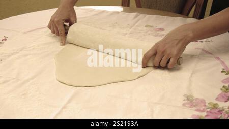 Woman rolling out dough on a table with her hands, sepia toned Stock Photo