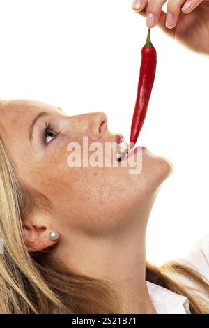 A young woman bites into a chilli pepper. Against a white background Austria Stock Photo