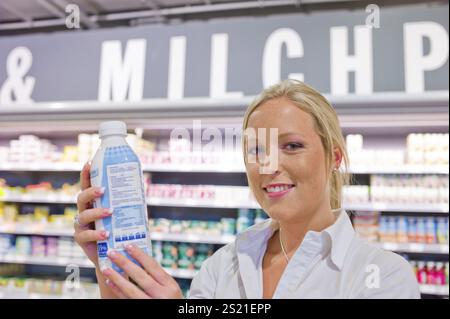 A young woman buys milk in the supermarket. Standing in front of the chiller cabinet. Austria Stock Photo