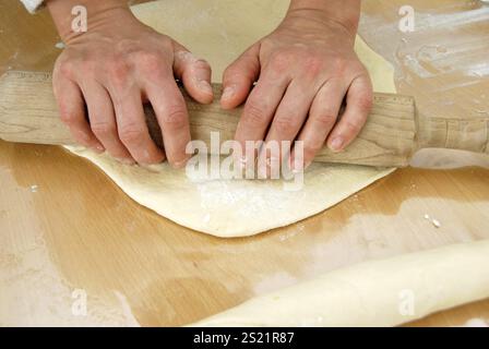 Woman rolls out dough on the table with her hands Stock Photo