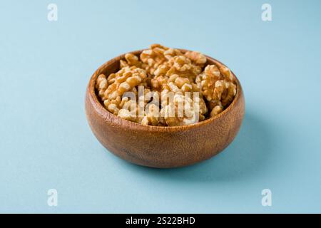 Top view of heap of walnut kernels in wooden bowl on blue background Stock Photo