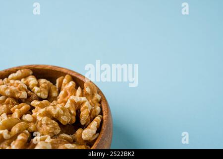 Top view of heap of walnut kernels in wooden bowl on blue background Stock Photo