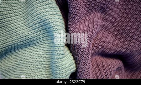 Background is filled with knitted fabric of different colors. Turquoise and purple. Clothing. Background is divided into two unequal parts by purple and turquoise knitted fabric. Hand made. Fashion. Stock Photo