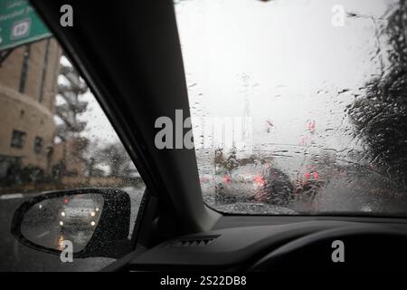 Out of focus cars their back lights on, traffic lights, traffic on a wet Jerusalem road, rainy day seen through rain drops on windshield & side mirror. Stock Photo