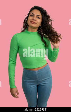 Fashionable millennial woman wearing green top and jeans posing on pink background Stock Photo