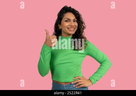 Smiling businesswoman showing thumbs up sign, expressing agreement or approval, on pink background Stock Photo