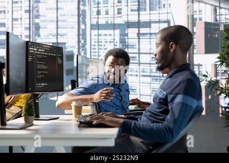 Manager in wheelchair checks on employee testing machine learning company software to minimize occurrence of bugs, identifying bottlenecks. Team leader with disability supervising worker writing code Stock Photo