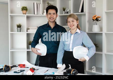 Architects Planning a Modern House Construction with Blueprints and Safety Helmets in a Contemporary Office Setting Stock Photo