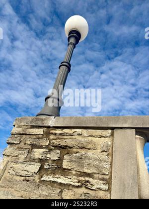 Close-up of a vintage lamp post atop a stone wall against a blue sk Stock Photo