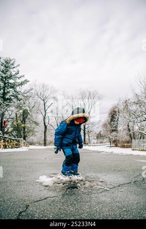 Child jumping in a snowy puddle on a winter road Stock Photo