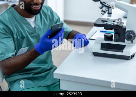 Scientist in laboratory conducting experiment and tests on samples using mobile phone and microscope Stock Photo