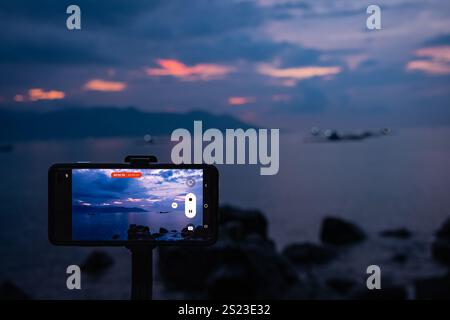 Cropped image of the phone taking photo in evening dusk of nature environment, modern smartphone camera on tripod capturing image. Smartphone video ti Stock Photo