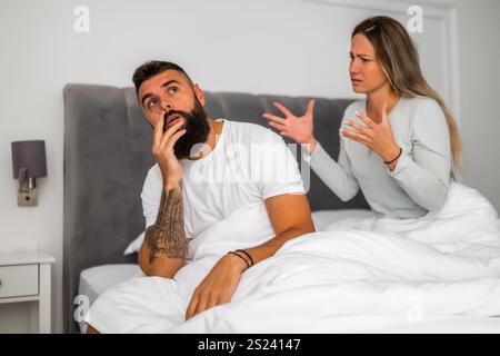 Couple is sitting in bed and arguing. The woman is angry with the man. Stock Photo