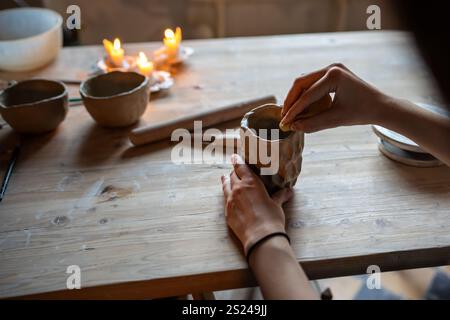 Womans hands wet and align clay cup with sponge on studio table. Handmade crockery, artisanal craft Stock Photo