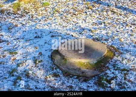 A round concrete pedestal rests on the ground, partially covered by a thin layer of snow in a serene outdoor location during winter. Stock Photo