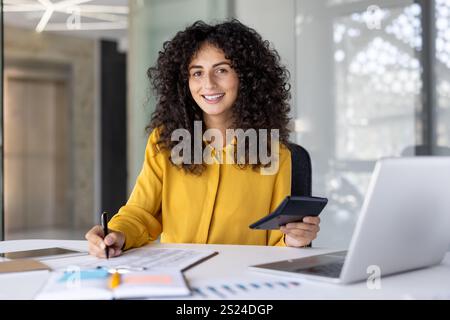 Paperwork, businesswoman writing data in spreadsheet and filling out tax forms, woman inside office using laptop, financier accountant preparing financial investment report, smiling looking camera Stock Photo
