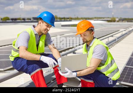Electricians Configuring Solar Panels On Roof With Laptop Stock Photo