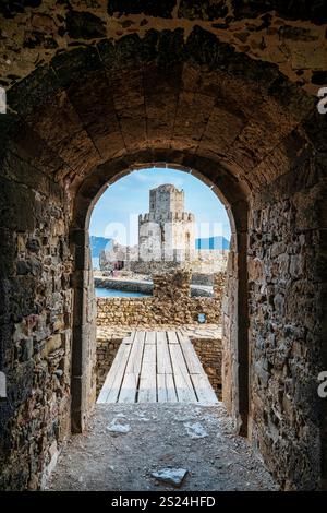 The iconic Bourtzi Tower at Methoni Fortress, viewed through a stone archway with a wooden bridge leading toward the historic structure. Stock Photo