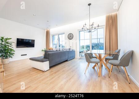 Contemporary living room featuring hardwood floors, sleek furniture, and a glass dining table, complemented by natural light from large windows. Ideal Stock Photo