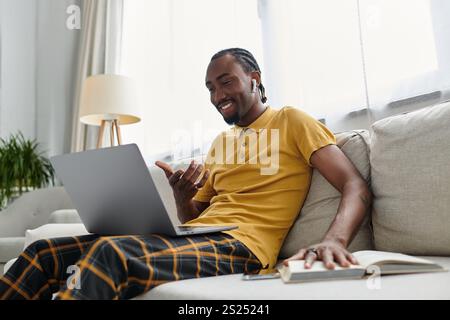 He smiles as he conducts a video call, merging work and comfort in a stylish living room setting. Stock Photo
