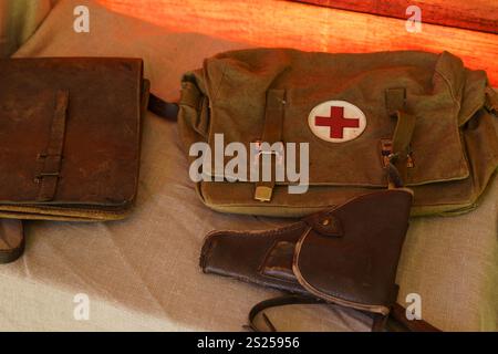 A collection of vintage medical supplies is displayed on a neutral surface, highlighting a green medical bag with a red cross, an old leather satchel, Stock Photo