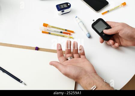Young man checks blood sugar with a meter while surrounded by diabetes management tools at home. Stock Photo