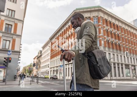 African American man using a smartphone while standing on the European city street with modern and historic architecture buildings. Stock Photo