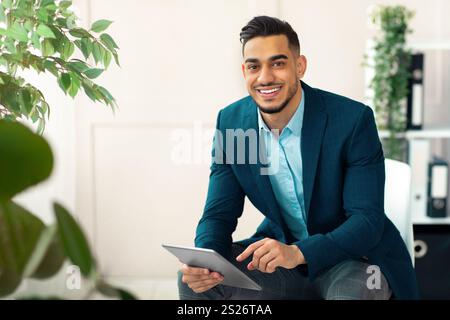 Handsome Arab businessman in formal suit using tablet pc at workplace, looking through web documents in office Stock Photo