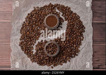 Fresh aromatic grain and ground coffee in transparent glasses on craft paper, wooden table. Composition in the form of yin yang Stock Photo