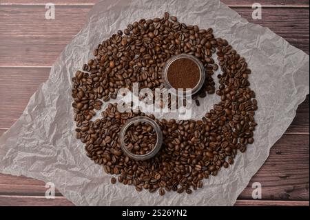 Fresh aromatic grain and ground coffee in transparent glasses on craft paper, wooden table. Composition in the form of yin yang Stock Photo